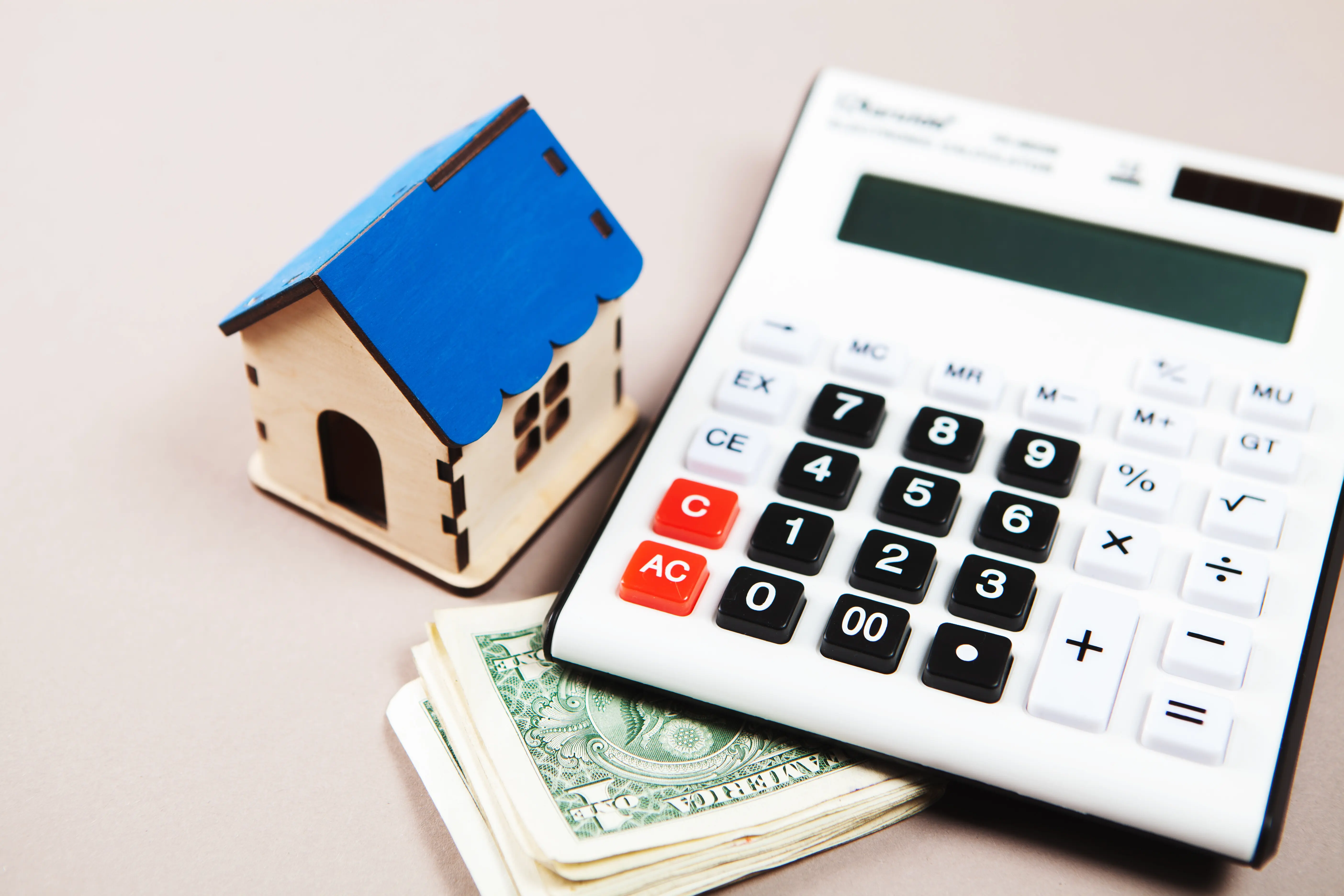 Auf dem Tisch liegen ein Haus, ein Taschenrechner und Geld – das Konzept, die Kosten des Hauses zu berechnen.